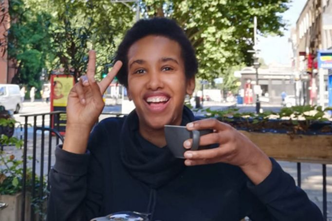 Student drinking coffee, giving the peace sign